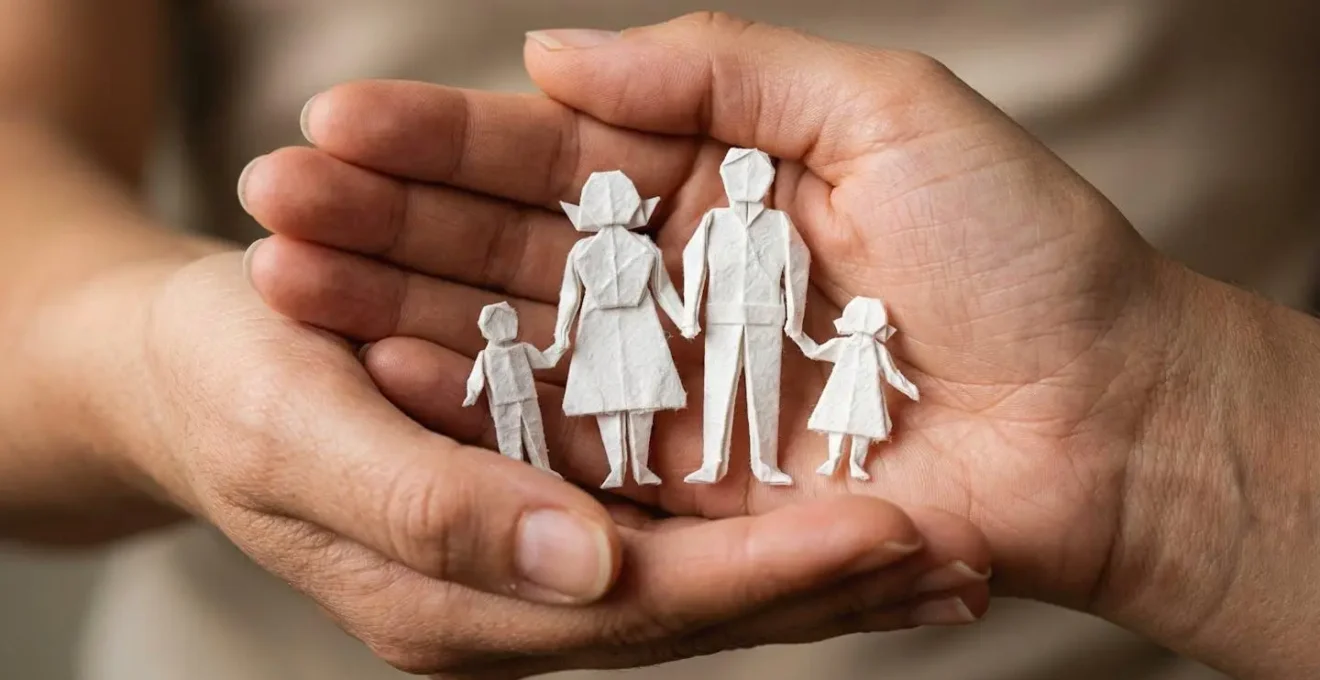 Mains protectrices formant un toit au-dessus d'une famille miniature en origami