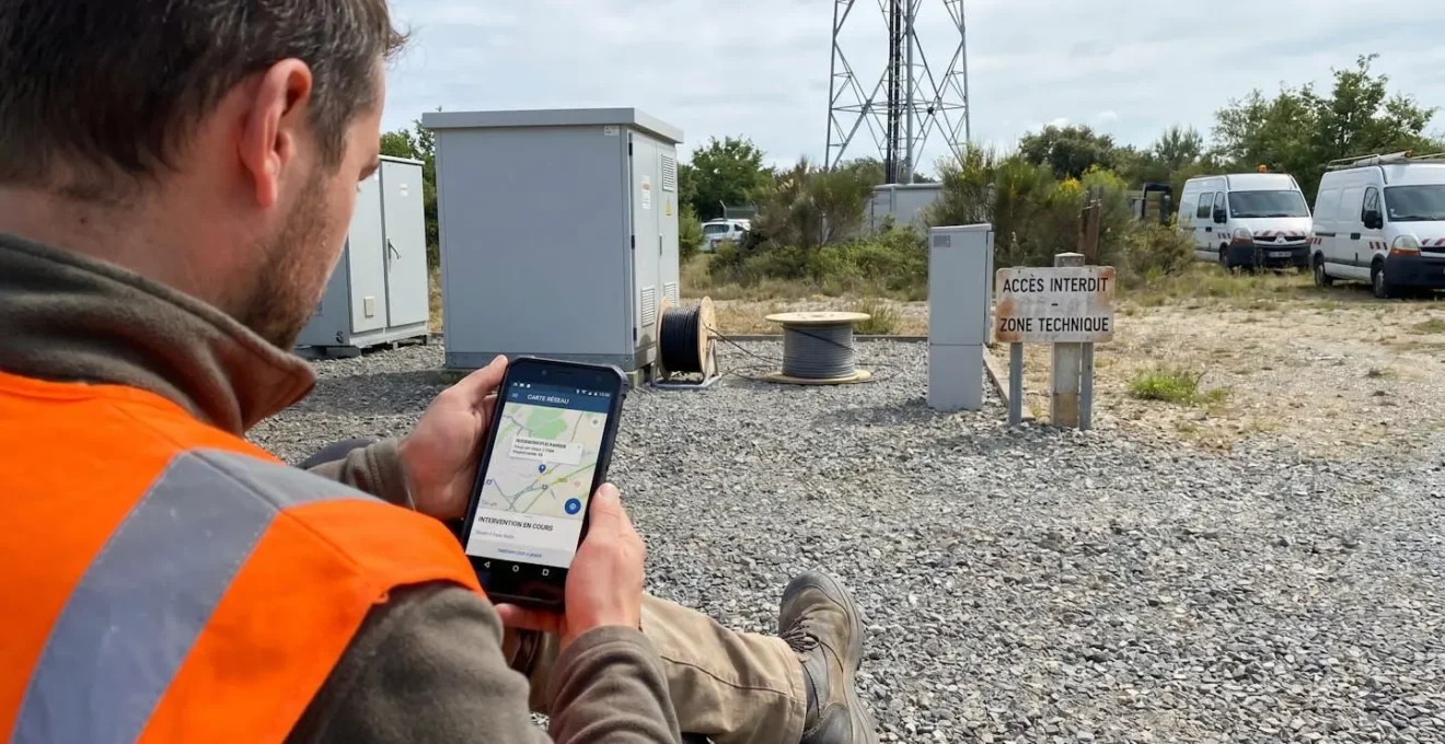 Technicien de dos en gilet de travail consultant une application sur smartphone lors d